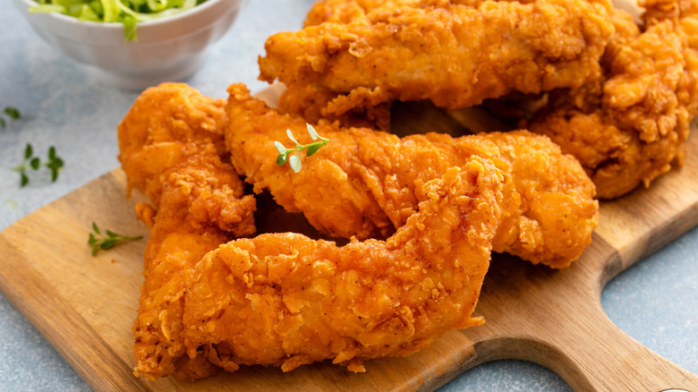 Chicken tenders on a wooden platter.