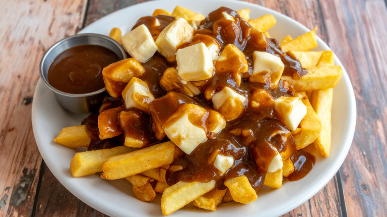 Poutine with small metal cup of brown gravy on a white plate