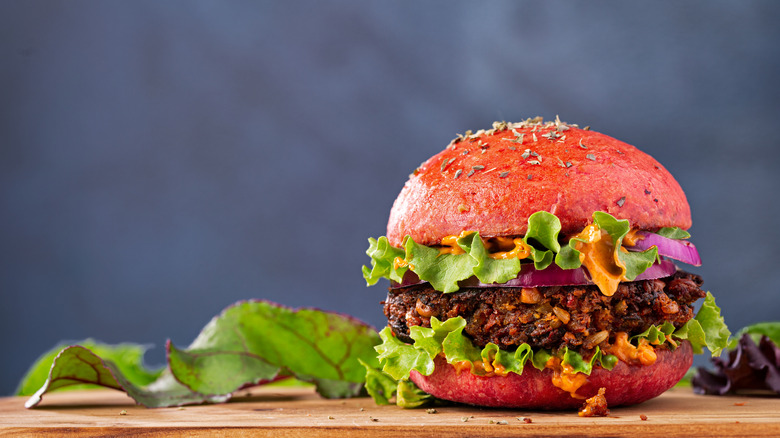 A veggie burger dripping burger sauce sits on a wooden cutting board with some rustic lettuce in the background