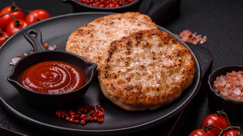 two ground chicken burger patties on a black plate wth ketchup