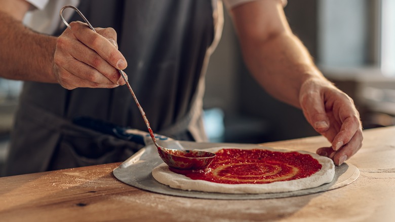 Pizza sauce ladled onto pizza dough