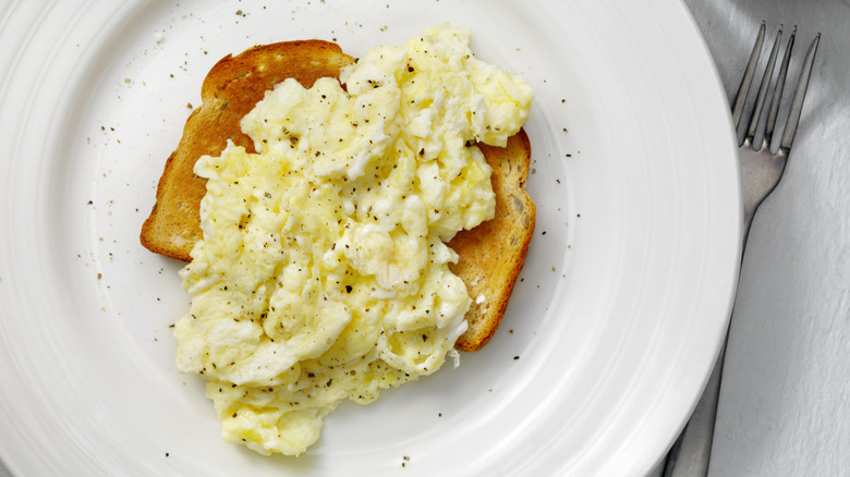 Scrambled egg with toast on white plate with fork