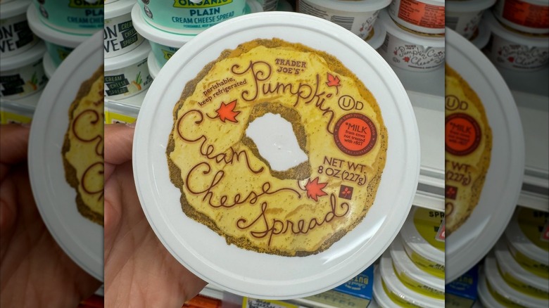 Someone holds up a container of Trader Joe's Pumpkin Cream Cheese Spread.