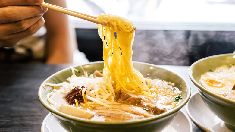 Person using chopsticks to eat from bowl of ramen