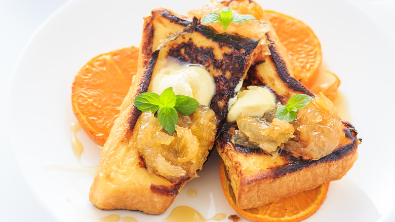 Sliced French toast rests on a plate, topped with caramelized orange, butter,and fresh mint