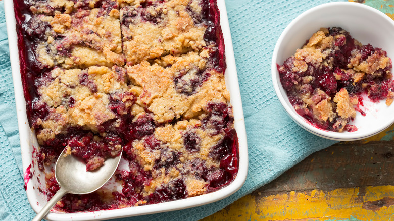 A cherry dump cake in a white cake pan with a dish of the dessert sitting adjacent