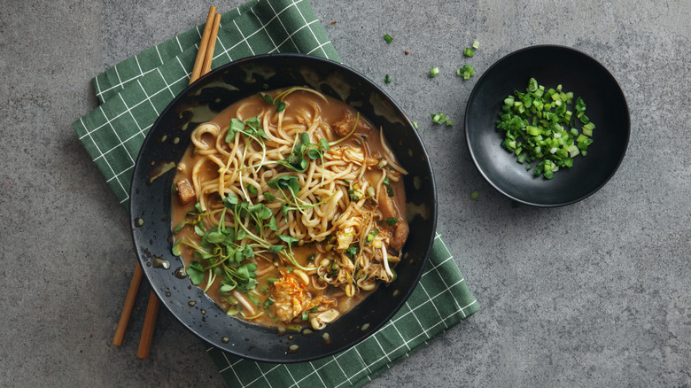 A chinese style chicken noodle oup topped with greens, with a side of scallions.