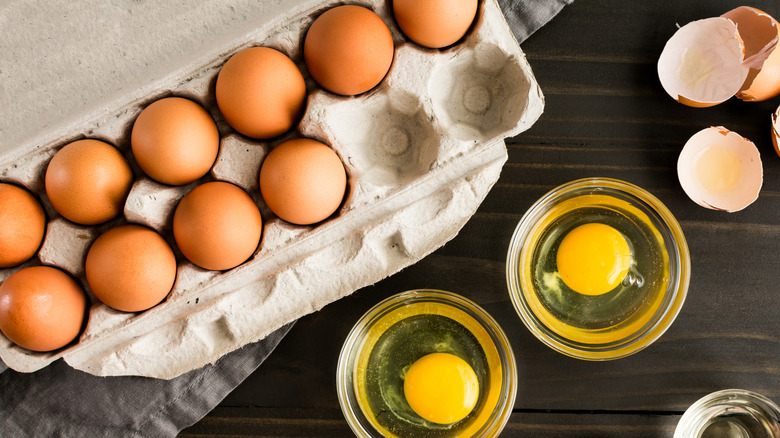 A carton of eggs with two cracked into small bowls.