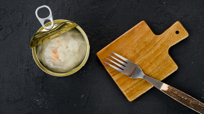 Canned crab meat next to a fork and small wooden serving board