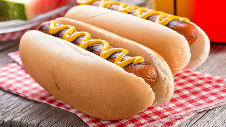 Two hot dogs dressed with mustard on checkered napkin