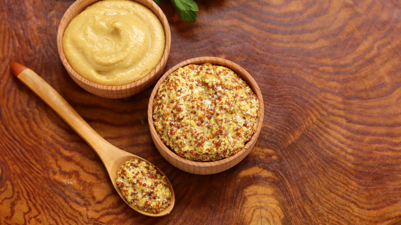 Two types of dijon mustard sit in bowls on a wooden table