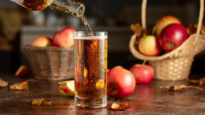 A glass of apple cider being poured with apples in the background.