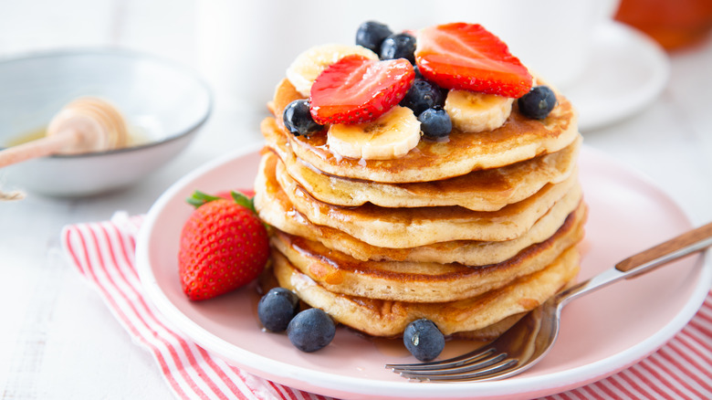 Stack of homemade pancakes topped with strawberry, banana, and blueberries.