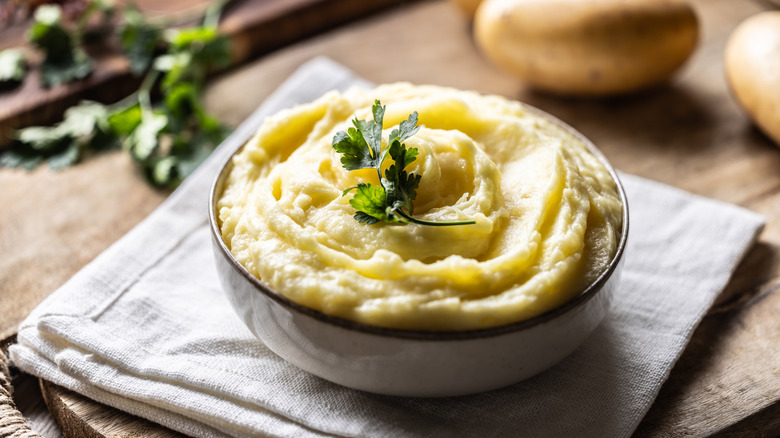 Mashed potatoes garnished with a parsley sprig in a small white bowl on a folded white cloth napkin