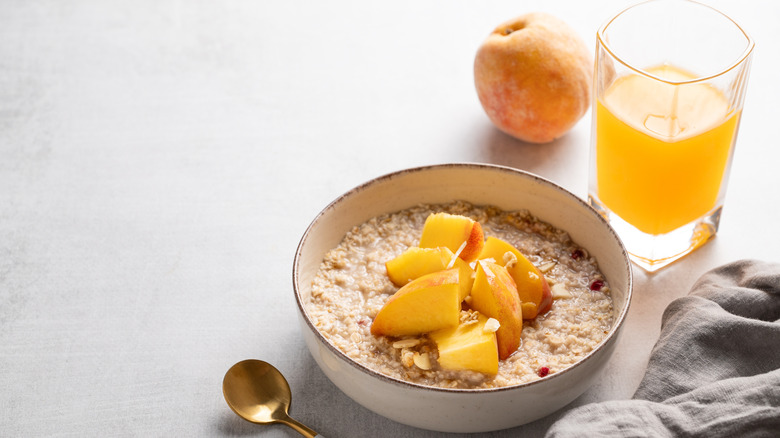 a bowl of oatmeal topped with chopped nuts and peaches next to a glass of orange juice