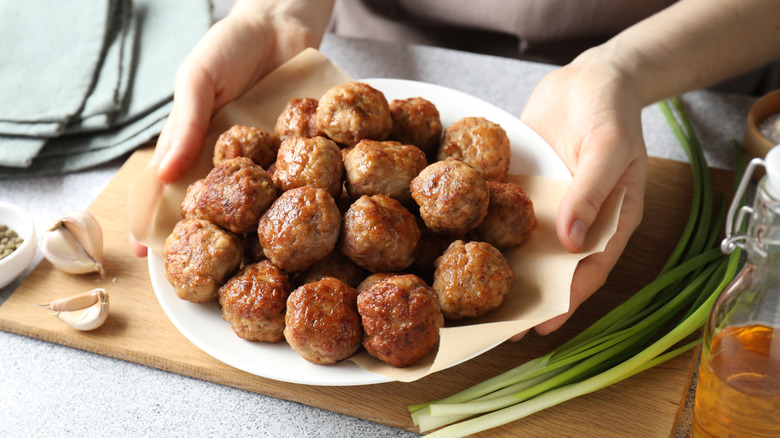 Someone holds a plate of meatballs.