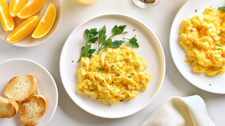 A plate of scrambled eggs in the center surrounded by cheesy scrambled eggs, toasted slices of French bread, and orange slices