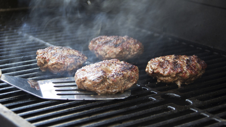 Thick burgers being flipped on the grill.