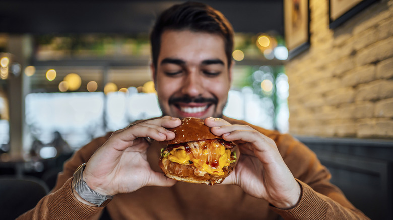 Person eating a burger, oozing cheese.