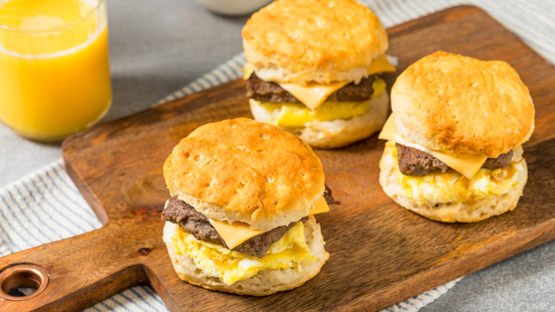 Sausage biscuits with egg and cheese on a platter next to a glass of orange juice