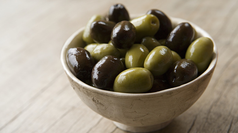 A stone bowl contains green and black olives