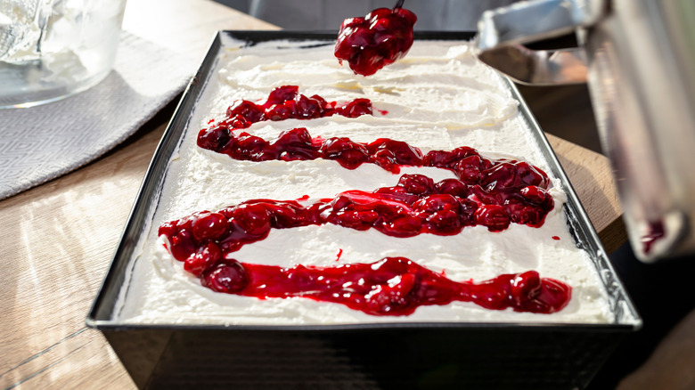 A home baker decorates a cake frosted with cream and cherry compote.
