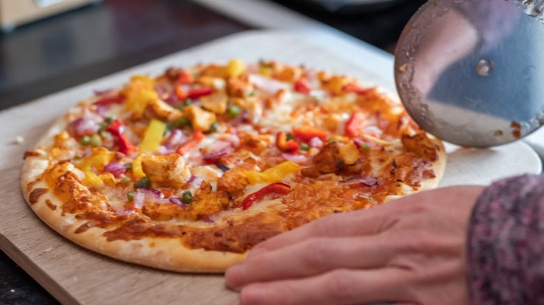 Hands cutting into a heavily-topped pizza with a pizza cutter