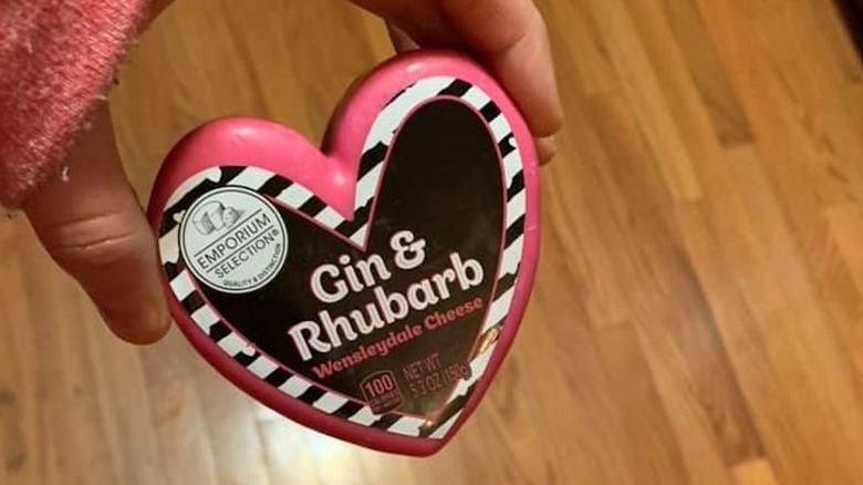 A hand holds a heart-shaped cheese over the kitchen floor