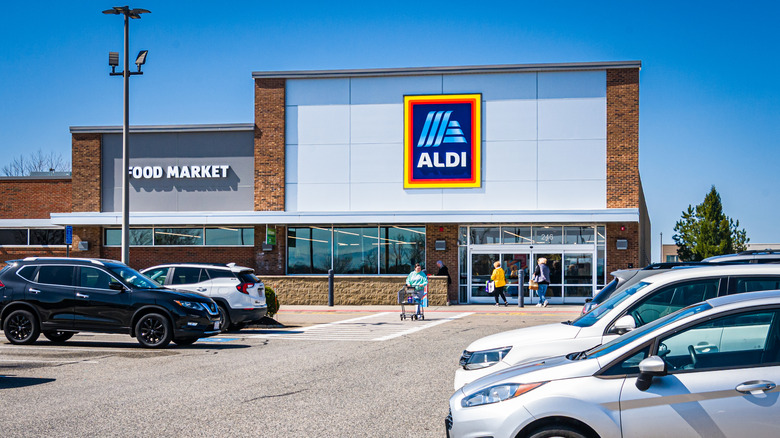 People entering and leaving with a shopping cart at the Aldi Food Market on a bright April morning.