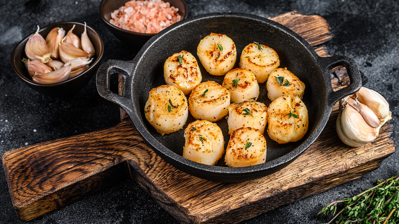 seared scallops in pan with garlic cloves in bowls