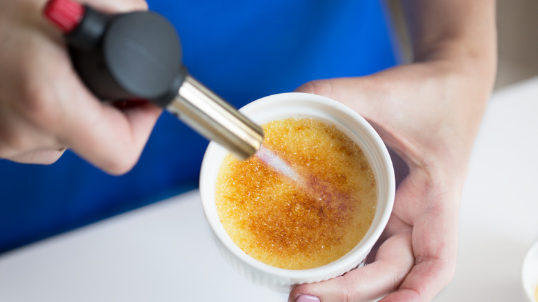 person torching the top of a creme brulee