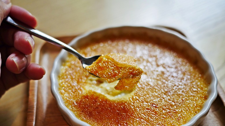 person breaking through creme brulee topping with spoon