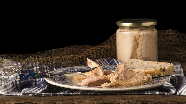 jarred tuna on a wooden table with a tuna sandwich