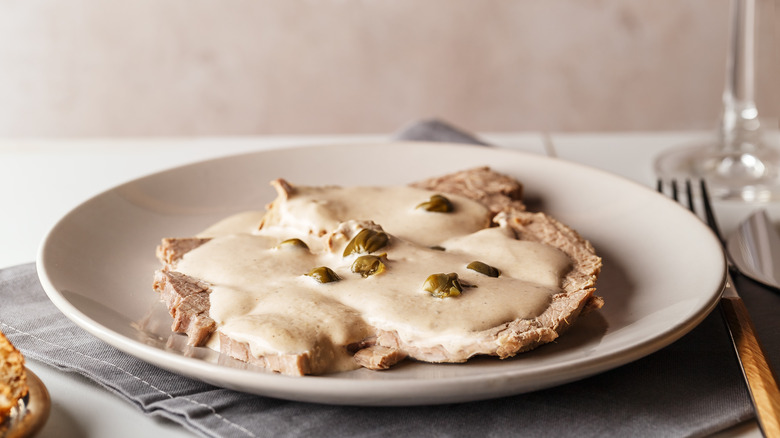 vitello tonnato with caper garnish on a white plate
