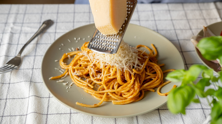 Cheese grated onto a spaghetti dish next to a fork, with basil in the foreground