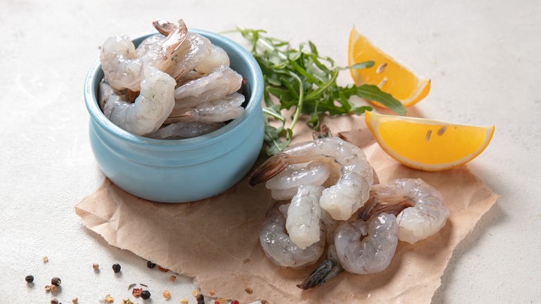 Raw shrimp in blue bowl next to citrus wedges