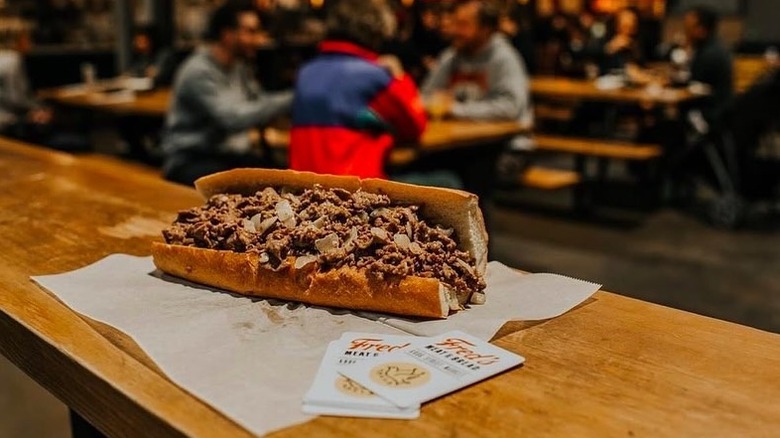 a cheesesteak from Fred's rests on a table as people dine in the background