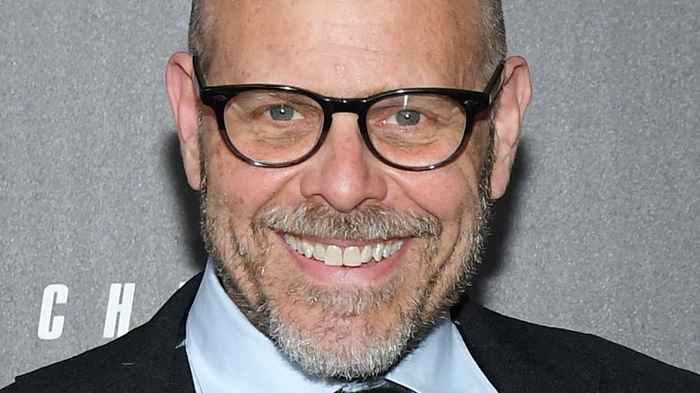 Alton Brown wearing black glasses, smiling on red carpet