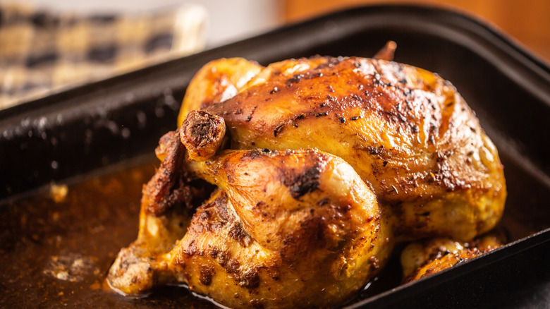A roasted chicken with crispy skin sits in a black pan
