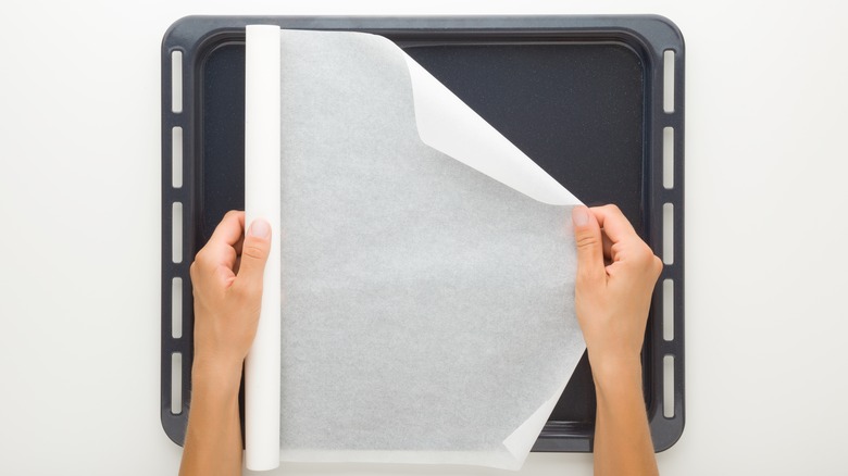 hands unrolling parchment over baking tray