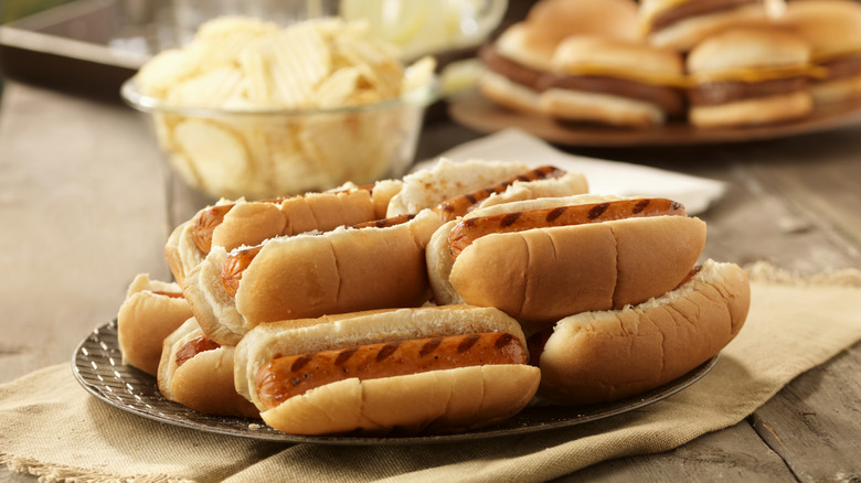 Hot dogs in buns on picnic table with burgers in back
