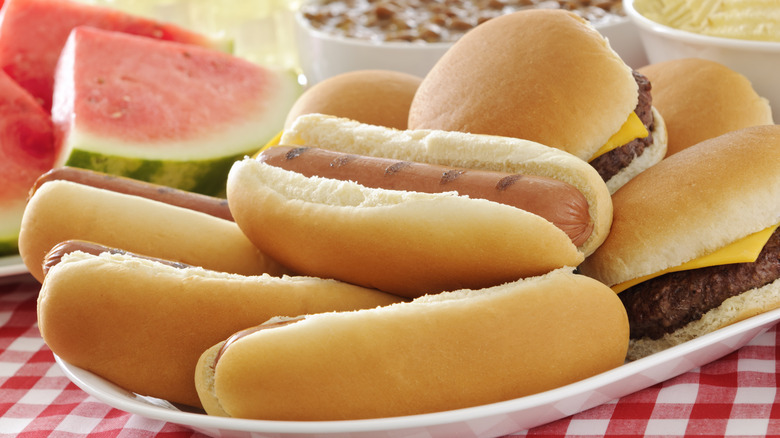 White platter stacked with hot dogs and burgers in buns