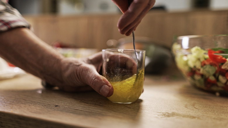 A cook uses a spoon to mix vinaigrette in a cup