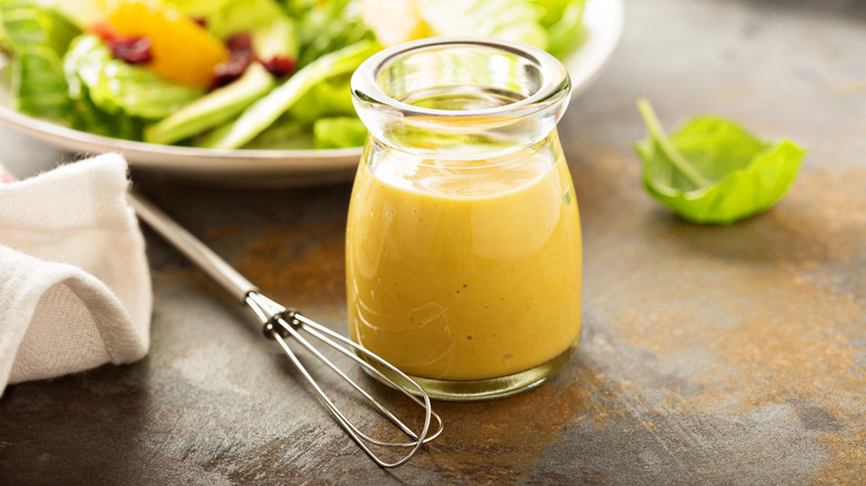 Creamy vinaigrette sits in a glass beaker in front of a salad