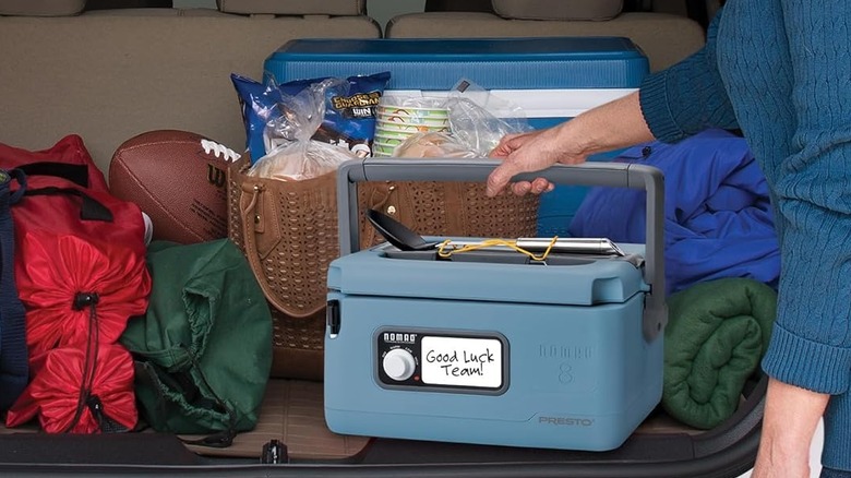 Someone lifts the Presto slow cooker out of the back of a cluttered car trunk