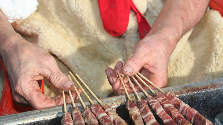 Close-up shot of an Italian man grilling meat on skewers.