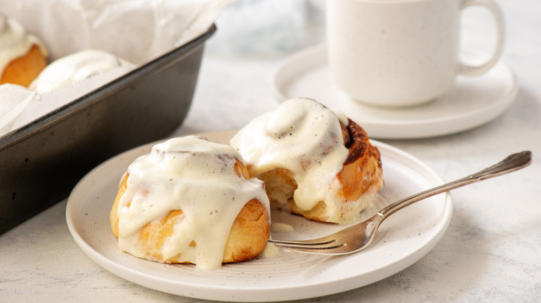 American style cinnamon rolls sit on a plate, slathered with cream cheese frosting.