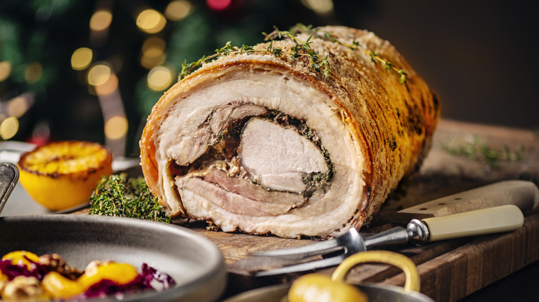 a juicy pork roast next to a grilled lemon, fresh  herbs, and potatoes