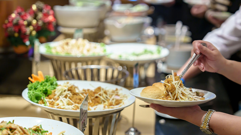 A diner spoons food onto a plate from a buffet.