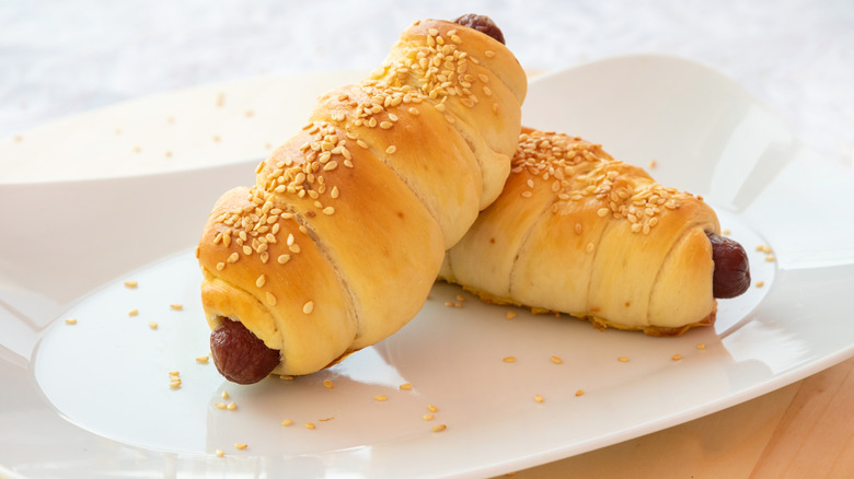 A pair of croissant hot dogs on a white plate
